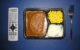 A TV dinner (meatloaf in gravy, corn, and mashed potatoes) in a black plastic tray, with a remote control to the left and silverware to the right. (Photo by John Atomic via Flickr/Creative Commons https://flic.kr/p/jKJNF)