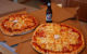 Two round pizzas, cut into square pieces, next to an open bottle of beer. (Photo by Jerry Huddleston via Flickr/Creative Commons https://flic.kr/p/9TLBjx)