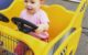 One year old is giggling as she "drives" a shopping cart that looks like a taxi.