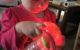 Baby girl looks intently at a glowing red ball while holding a red rattle.