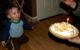 One year old is smiling as he looks at his birthday pie, which has banana pieces on top of whipped cream, plus a birthday candle.