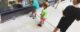 Two year old makes a shhh sign with his hand. He, his sister and his brother are all looking at a gray tabby cat sleeping in a store window.