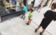 Two year old makes a shhh sign with his hand. He, his sister and his brother are all looking at a gray tabby cat sleeping in a store window.