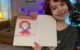 Six year old holds up a picture of her three-eyed, red-haired alien person named Bubblegum.