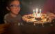 Middle kid smiles as he looks at the candles on his birthday cake.